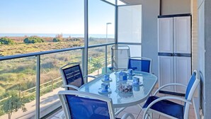 A balcony with a glass table set for two, overlooking a coastal landscape.