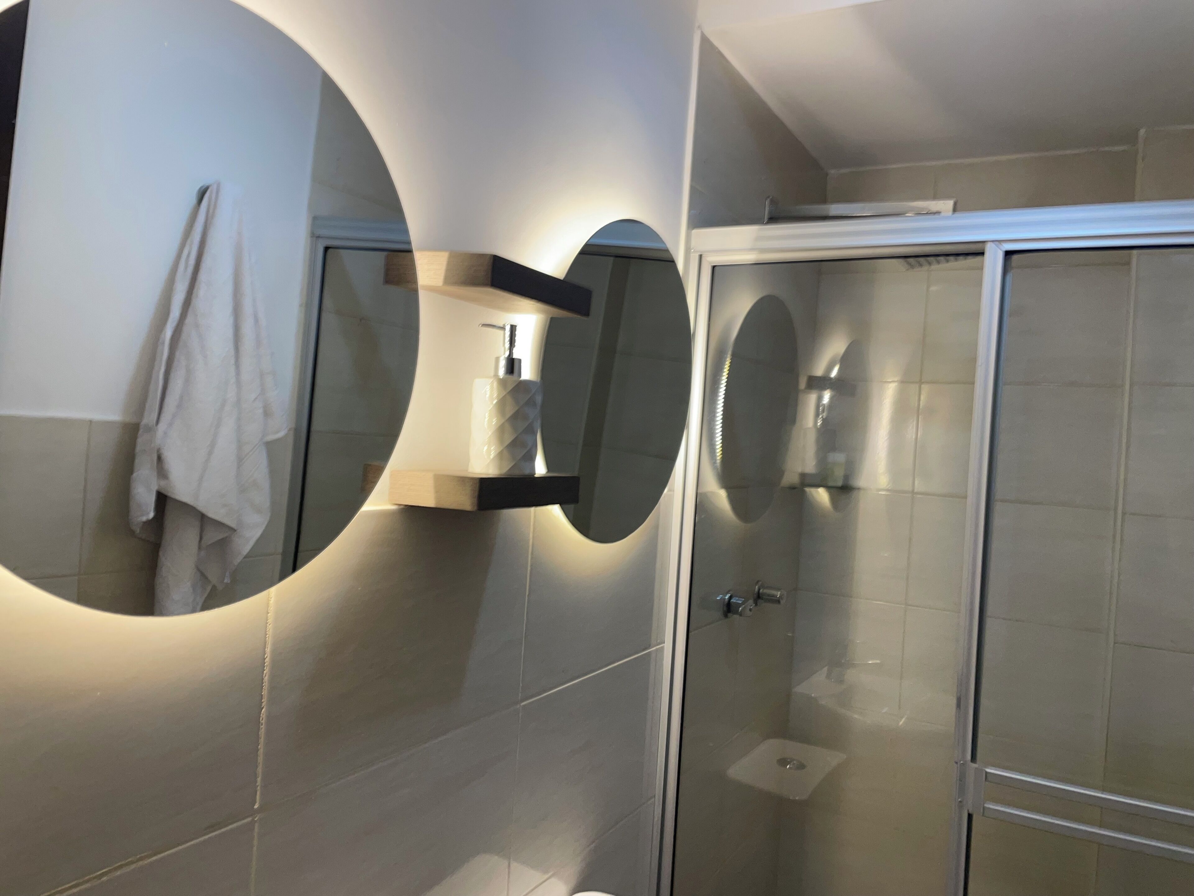 Une salle de bain moderne dotée d’une douche à parois de verre, d’un grand miroir avec éclairage intégré et d’un porte-serviettes.