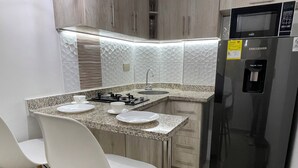 A compact kitchen with a built-in microwave, a water dispenser, and a gas stove. There are two white chairs and a small island with a sink. - Luxury Liv Limonar (Cali)
