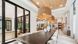 A spacious dining area with a long wooden table, white chairs, and a large woven pendant light. - The Palm House at Reunion-TT484 (Kissimmee)
