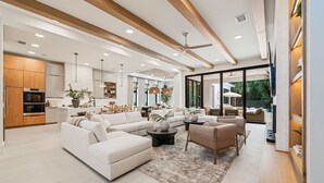 A modern living room with a sectional sofa, coffee table, and a dining area with a chandelier. - The Palm House at Reunion-TT484 (Kissimmee)