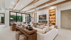 A spacious living area with a large sofa, a wooden coffee table, and a fireplace. There is a bookshelf with decorative items and a large painting on the wall. - The Palm House at Reunion-TT484 (Kissimmee)