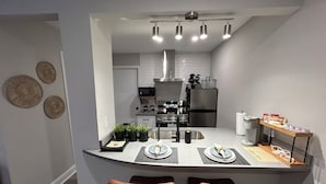 Una cocina moderna con una isla central, dos sillas, un microondas, un refrigerador y una lámpara colgante.