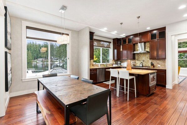 A modern kitchen with wooden cabinets, a large island, and a dining area with a wooden table and chairs.