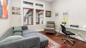 A modern living room with a grey sofa, a small armchair, a glass desk, and a chair. There are framed pictures on the wall and a window with blinds. - Luxury Lake Waterfront Friendly Retreat (Federal Way)