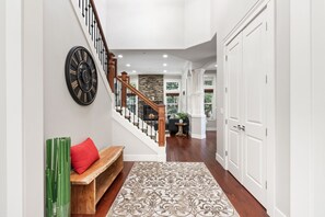 A staircase with a wooden handrail and black balusters, leading to a room with a stone fireplace and a view of greenery outside.