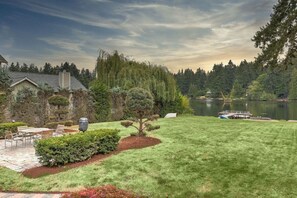 A well-maintained lawn with a patio area, a small tree, and a view of a lake with a dock.