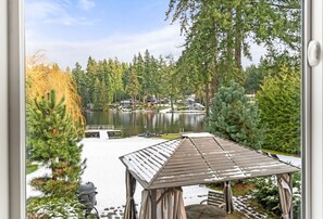 A gazebo with a snow-covered roof overlooking a lake, surrounded by trees and a dock.