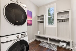 A laundry room with a Samsung washer and dryer, a window with a view of trees, and a shelf with towels.