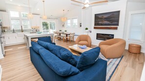 A modern living room with a blue sofa, a brown armchair, and a dining area with a table and chairs. - Oceanside, ELEV, Priv Pool, Comm Amenities, Dogs Welcome-BH7, O'Buoy (Corolla)