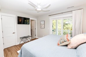 Une chambre à coucher avec un lit, un ventilateur de plafond, une fenêtre avec des rideaux et une porte.