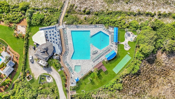 Vue aérienne d’un complexe hôtelier doté de plusieurs piscines, d’un court de tennis et d’une végétation luxuriante.