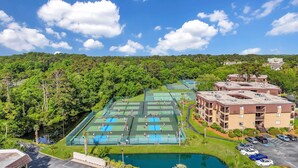 Un complexe de courts de tennis entouré d’une végétation luxuriante, situé à côté d’un immeuble à plusieurs étages doté d’un parking.