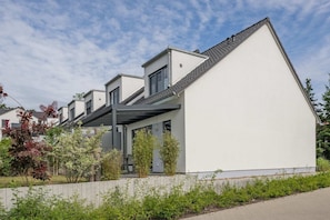 Un immeuble résidentiel moderne avec une façade blanche, un toit en pente et un espace extérieur couvert.