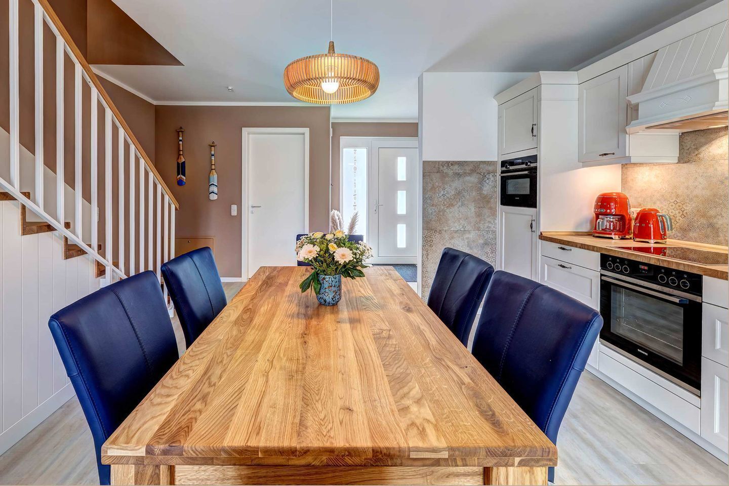 A modern kitchen with white cabinets, a wooden dining table, and blue chairs.