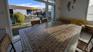 A spacious room with a large table, a sofa, and a view of the outside patio area. - The Fleur de Sel - 6 people (Les Sables-d´Olonne)