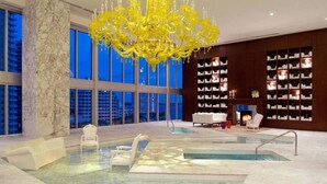 A modern indoor pool area with a large chandelier, seating, and bookshelves.