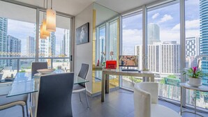 A modern office space with a glass table, chairs, a desk with a computer, and a large window offering a city view.