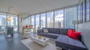 A modern living room with a grey sofa, a white coffee table, and a city view through large windows.