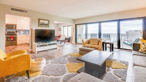 A modern living room with a flat-screen TV, comfortable seating, a dining area, and a balcony with a view. - Top-floor Condo w/ Stunning Views, 2 Pools & More (New Smyrna Beach)