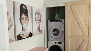 Een compacte leefruimte met een wasmachine, een roze kast en een eethoek met een marmeren tafel.