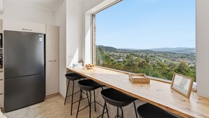 A modern kitchen with a large window, a black refrigerator, and a wooden countertop with bar stools. - MONA Vista, overlooking Museum of Old and New Art (MONA) & the River Derwent. (Rosetta)