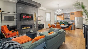 Un salon moderne doté d’une cheminée, d’un coin repas et d’une cuisine avec des meubles en bois et des appareils électroménagers en acier inoxydable.