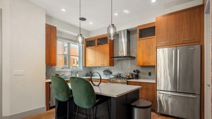 Une cuisine moderne avec des meubles en bois, un réfrigérateur en acier inoxydable et un coin bar avec des chaises vertes.