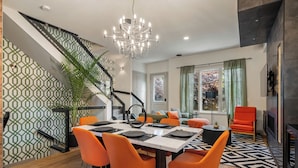 Un espace de salle à manger moderne, agrémenté d’un lustre, de chaises orange et d’un mur orné d’un motif géométrique.