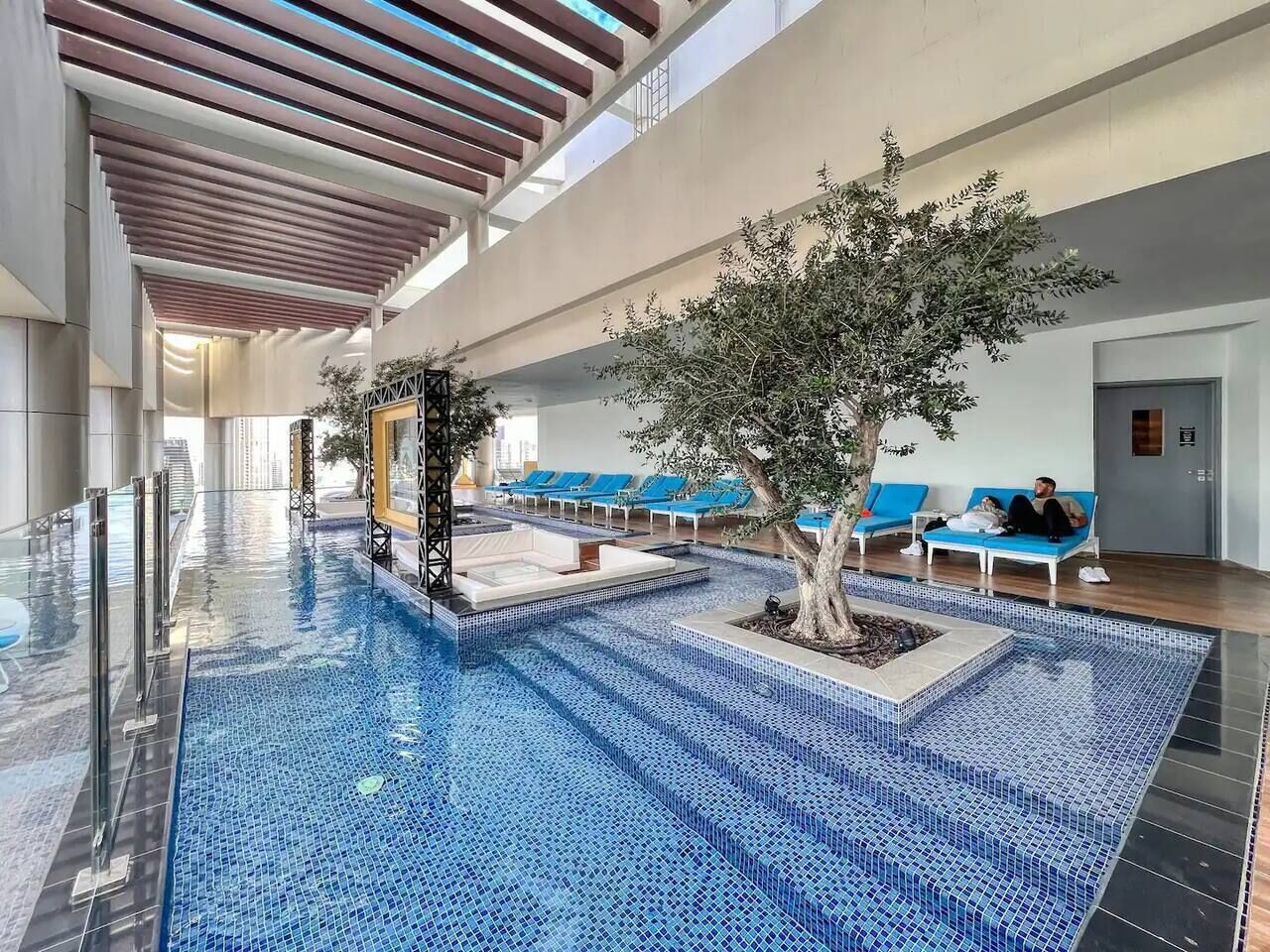 Ein Innenpool mit blauen Mosaikfliesen, Liegestühlen und einem Baum.