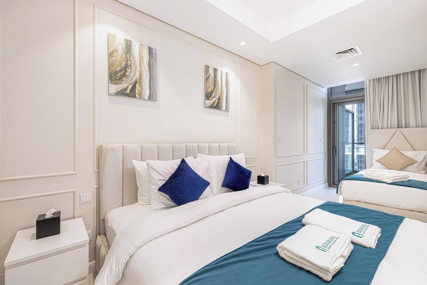Camera d'albergo con due letti, un'ampia finestra e opere d'arte alle pareti.