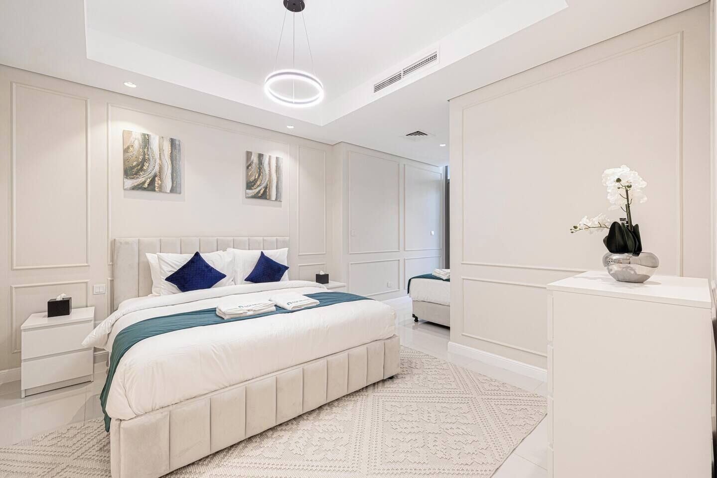 Un dormitorio moderno con una cama grande, mesitas de noche y un jarrón decorativo sobre una cómoda.