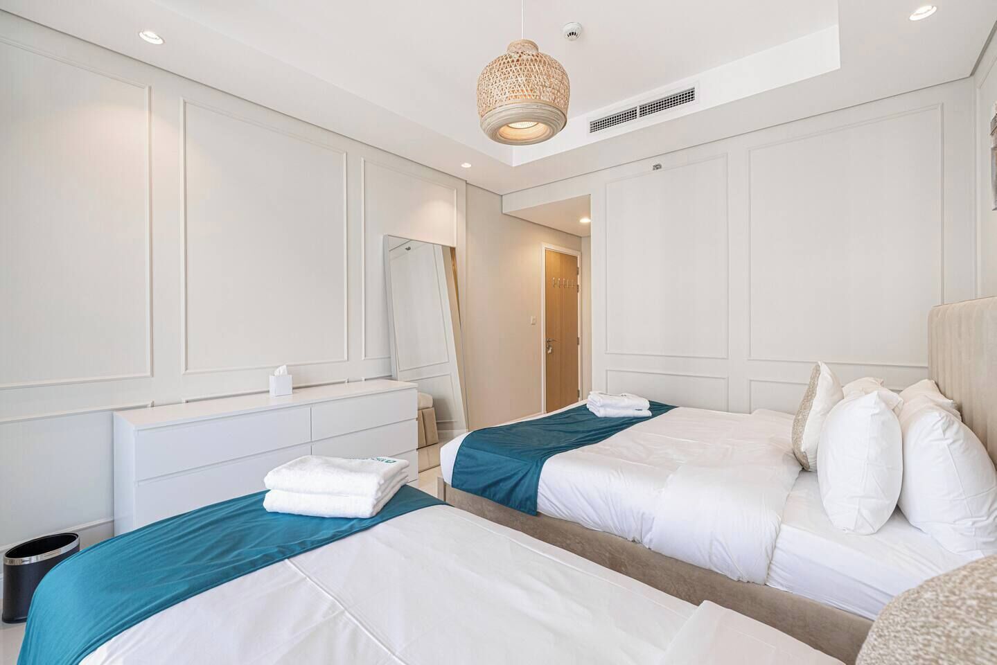A hotel room with two beds, a mirror, and a hanging light fixture.