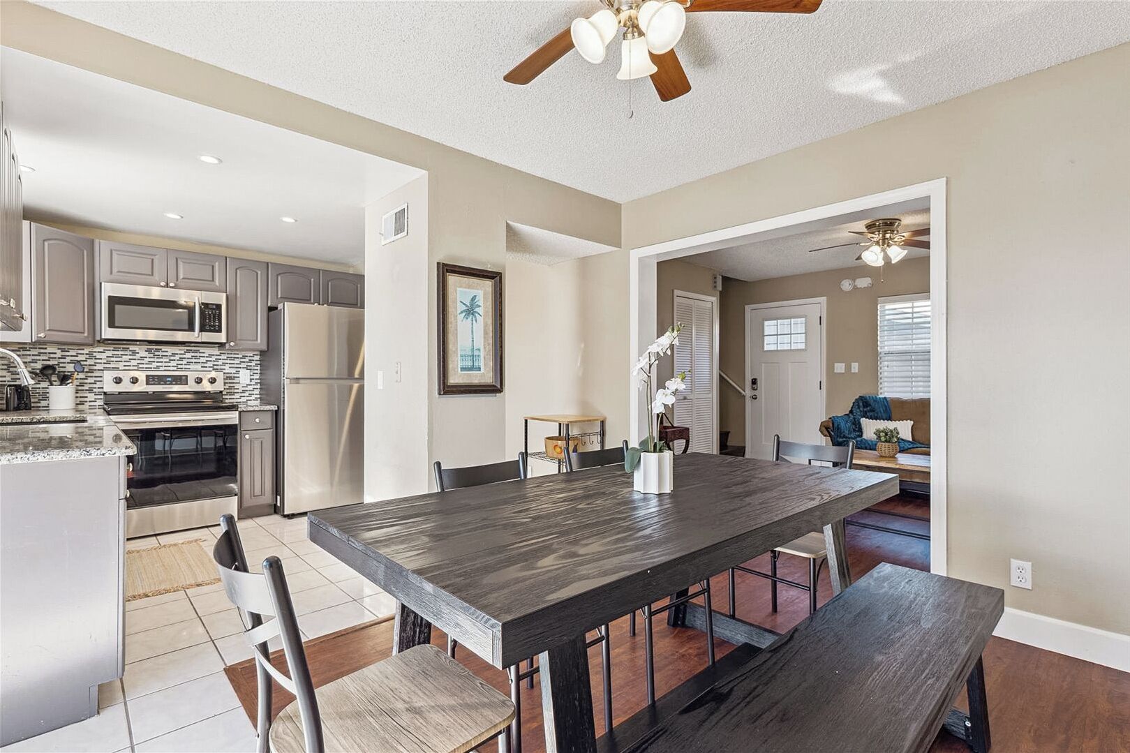 A modern kitchen with stainless steel appliances, a dining area with a dark wood table and chairs, and a ceiling fan.