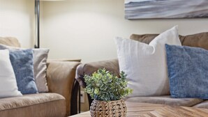 Una sala de estar con un sofá color beige, una maceta tejida y un cuadro con una playa.