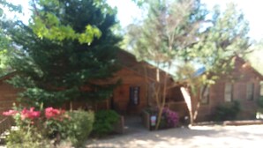 A rustic building with a brick exterior, surrounded by greenery and flowering plants. - Cozy 4-bedroom cabin with AC, fitness room, WiFi in fantastic Modoc (Modoc)