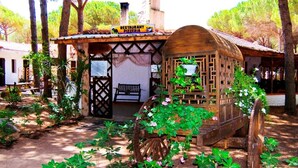 Une construction rustique en bois, identifiée par une enseigne comme restaurant et pizzeria, entourée de verdure et d’arbres.