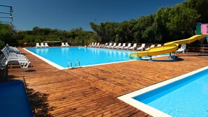 Une piscine avec une terrasse en bois, des chaises longues et un toboggan aquatique.