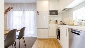 Cocina compacta con refrigerador, microondas, horno y lavavajillas. Hay un comedor con mesa y sillas.