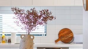 Una cocina moderna con armarios blancos, una mesa de comedor de madera, sillas negras y un jarrón decorativo con flores rojas.