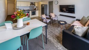 Una sala de estar moderna con comedor, cocina y televisor montado en la pared.