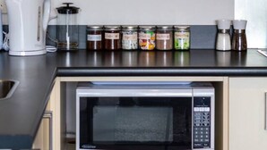 Una cocina compacta con microondas integrado, cafetera y varios frascos sobre la encimera.