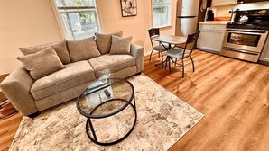 A cozy living area with a sofa, coffee table, and chairs, a kitchen with appliances, and large windows.