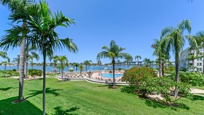 A pool area with palm trees, a bridge, and a view of the sea.