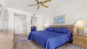 A bedroom with a bed, wooden nightstands, a ceiling fan, and a painting on the wall.