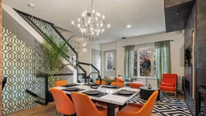 Un espace de salle à manger moderne, agrémenté d’un lustre, de chaises orange et d’un mur orné d’un motif géométrique.