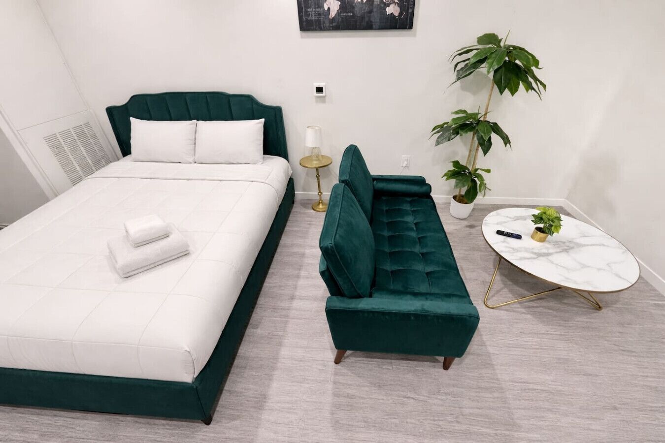 A modern bedroom with a bed, a green sofa, a small round table, and two potted plants.