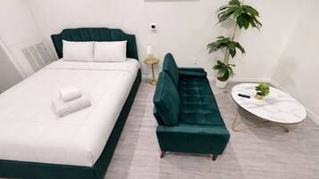 A modern bedroom with a bed, a green sofa, a small round table, and two potted plants.