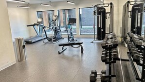 Un gimnasio con cintas de correr, elípticas, una banca y un estante con mancuernas.