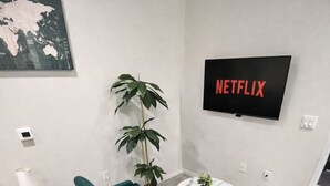Una habitación de hotel moderna con un sofá azul verdoso, una mesa de centro redonda, una planta en maceta, un televisor montado en la pared y un mapa del mundo.